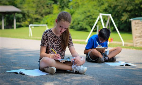 students write on clipboards outside
